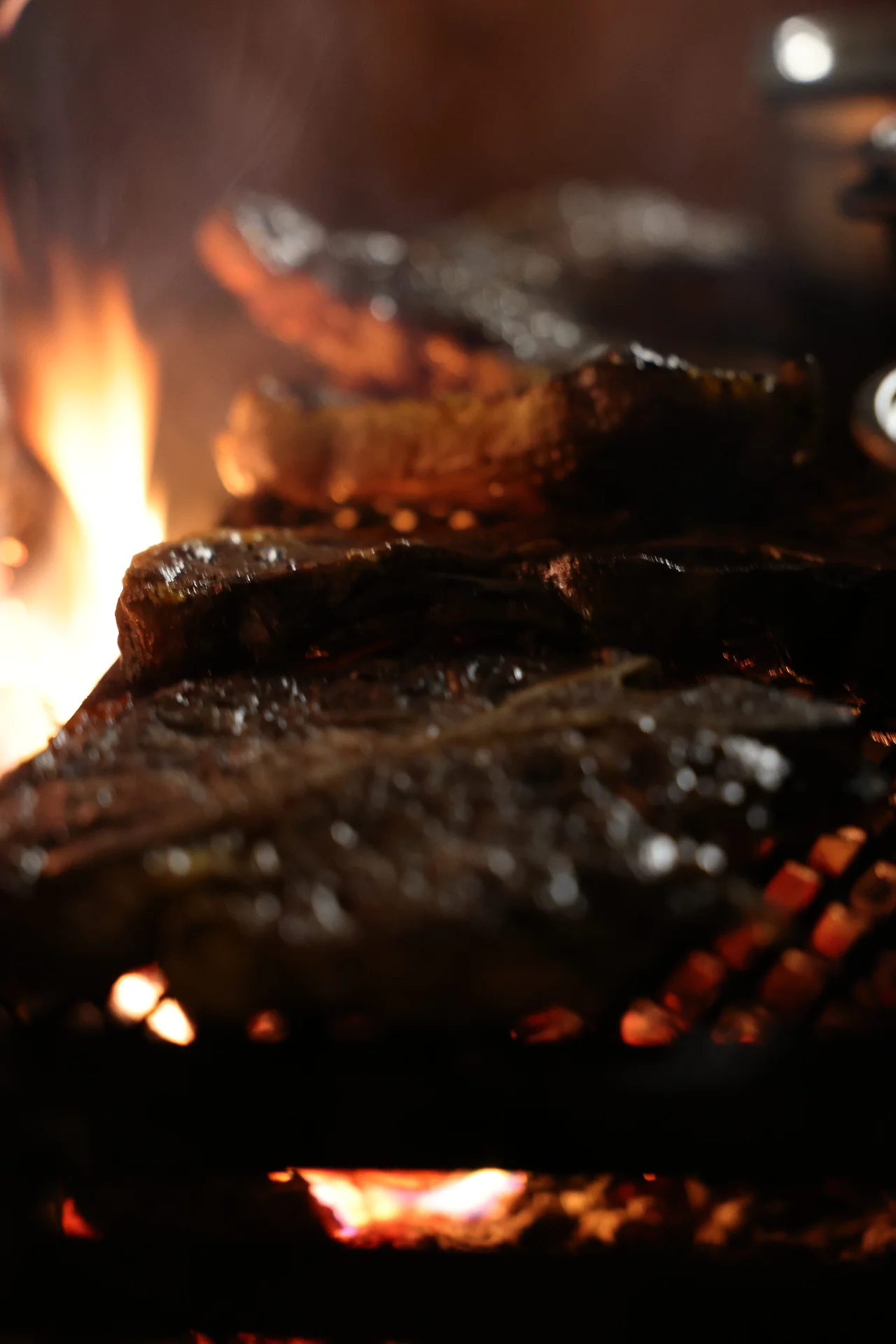 Steaks searing over open flame in the wood-fired grill